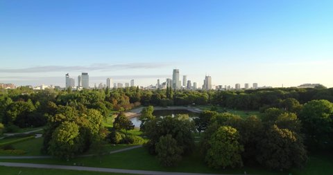 City park with the city center in the background. Aerial view of offices in skyscrapers over the panorama of Warsaw in a urban park. Lake in the park with green trees during summer.