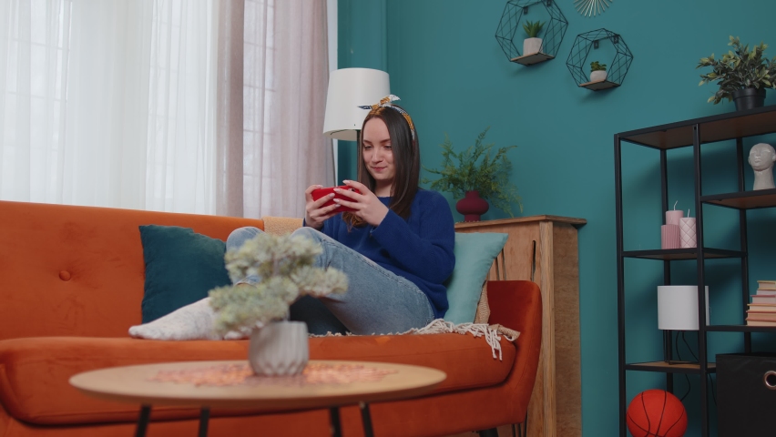 Worried funny addicted woman enthusiastically playing racing video games on mobile phone at home in living room on sofa. Young adult teen girl using smartphone gadget app with drive simulator isolayed