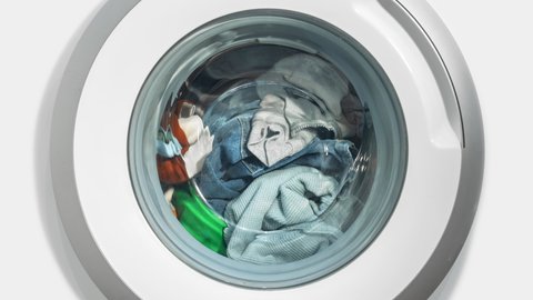 Timelapse white domestic washing machine, laundry machine wash colored clothes time-lapse shot. Washing clothes. Motion blur round drum, spinning circle on white background. Zoom out