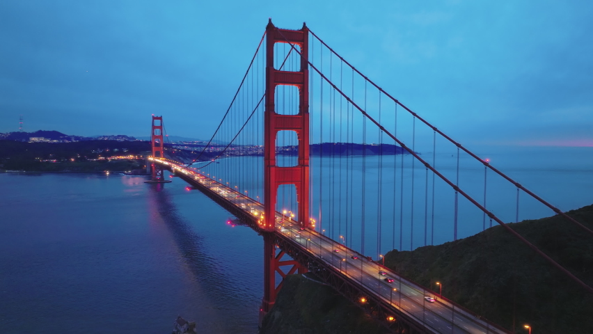San Francisco landmark at sunset on cloudy day, close up aerial view of the Golden Gate Bridge and city skyline. Cinematic drone footage of red bridge with night illumination on blue sky background 4K Royalty-Free Stock Footage #1088623885
