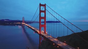 San Francisco landmark at sunset on cloudy day, close up aerial view of the Golden Gate Bridge and city skyline. Cinematic drone footage of red bridge with night illumination on blue sky background 4K