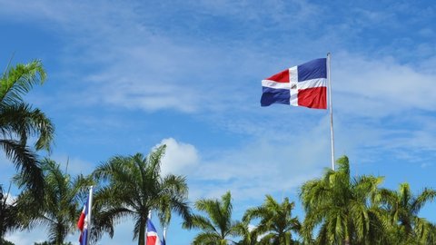 Flying and waving flag of Dominican Republic on wind on blue sky background