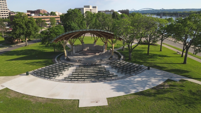 Drone view of park venue along Mississippi River in La Crosse, Wisconsin. Timber beams holding roof over stage venue. Benches in semi circle. Sun casting beautiful shadows. 