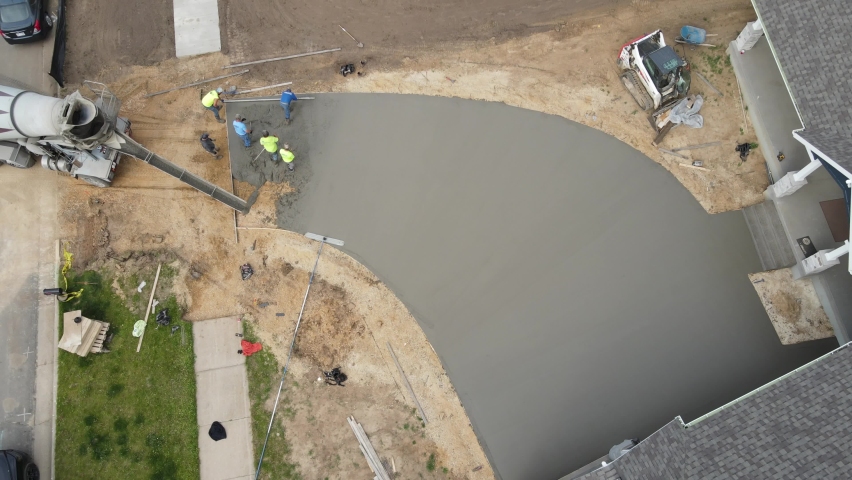 Birds eye view of concrete being poured to complete a new driveway. Crew working together to complete task. Gravel and dirt as base layers. New residential building project.  Royalty-Free Stock Footage #1088624883