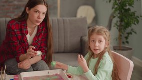 Little girl talks to elder sister coloring eggs for Easter holiday with Ebru design recording blog at home slow motion. Family vlog of art hobby
