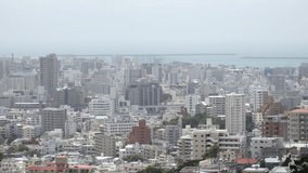 NAHA, OKINAWA, JAPAN - AUGUST 2021 : Aerial high angle wide view of Naha city in daytime. Cityscape of downtown area and sunny blue sky. Summer holiday, vacation and travel concept video.