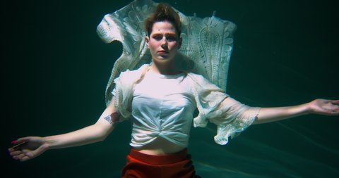 Amazing underwater portrait, young beautiful short haired happy blonde woman posing in elegant boho clothes slow motion.
