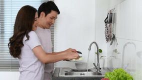 happy young couple dancing and washing dishes together in the sink in the kitchen at home. 4k Video.