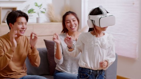 Happy Asian family spending time together. Father and mother cheer up their child to dance while wearing VR headset and dan.  All playing enjoy virtual reality goggles, modern technology glasses.
