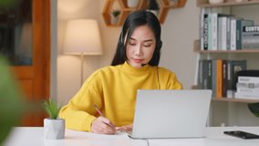Young Asian woman wearing headphone studying online education at home via laptop