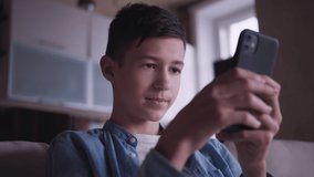 teen boy sits on the sofa and uses the phone, chatting with friends, playing a game, cinematic shot