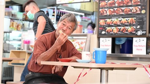 Singapore - 27th March 2022: A Chinese man is having his breakfast in Chinatown.