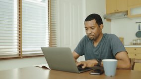 Concentrated Black African American man using laptop computer at dining table, Work from home, Freelancer typing on keyboard, Lifestyle