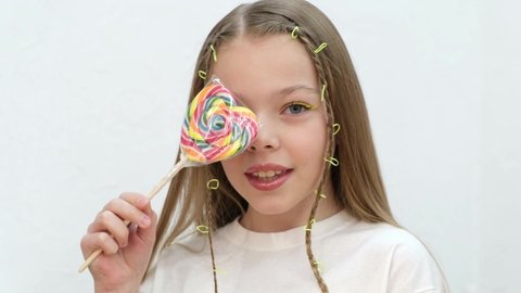 Cute little girl with colorful lollipop in the form of heart posing at camera.