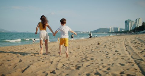 Happy caucasian children run forward along the beach. Little children brother and sister run along the beach, playing, family vacation. The concept of a beach holiday for young children