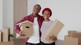 Moving New House. Happy African American Spouses Holding Moving Boxes Hugging Posing Smiling To Camera At Home. Housing For Young Family And Real Estate Purchase Concept