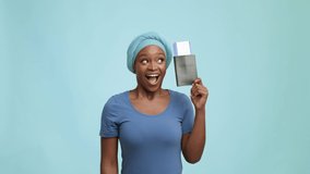 Vacation. Joyful Black Woman Shaking Travel Tickets Holding Passport And Boarding Pass Posing Over Blue Studio Background, Wearing Headwrap And Smiling To Camera. Traveling And Transportation