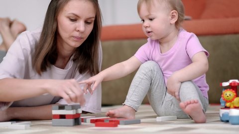 Little baby girl and mommy playing color wooden toys at home sitting on floor, Mother and daughter laughing having fun together
