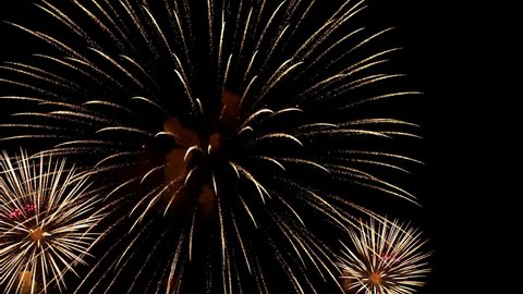 Slow-motion footage of large golden shimmering fireworks balls in the night sky, pyrotechnic rockets explode with yellow lights and smoke in the night.