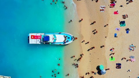 View of Navagio beach, Zakynthos Island, Greece. People relaxing on the beach during their vacation. Blue sea water. A boat drops people off at the seashore. Summer landscape from the air.