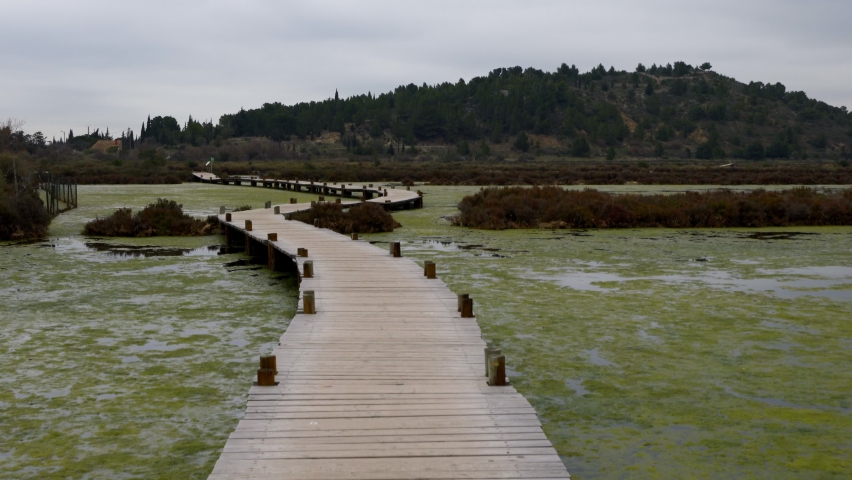 Walkway on a pond full of algae on a natural reserve on the south of France with Bages village on the background