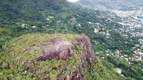 Aerial footage of Lion rock towering over the surrounding rainforest in Mahe, Seychelles 