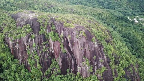 Aerial footage of Lion rock towering over the surrounding rainforest in Mahe, Seychelles 