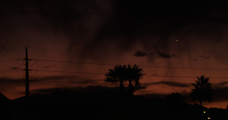 Hauntingly apocalyptic vision with wavering rain shafts, palm trees, transmission towers and and approaching airliners in silhouette against a menacing sky at dusk. 