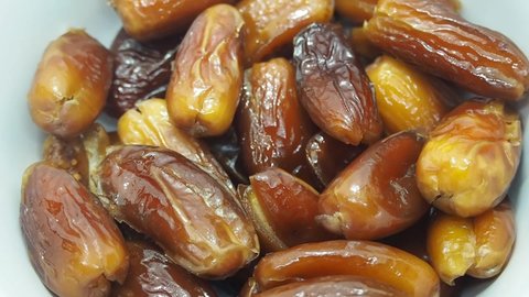 Footage full HD 1080P close up. A pile of dates in a white cup slowly spins. Tropical plants.