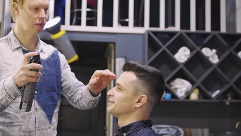 the hairdresser styling a brunette man and spraying hairspray in a barbershop. professional services. beauty salon for men. cosmetics and products for scalp and hair care.