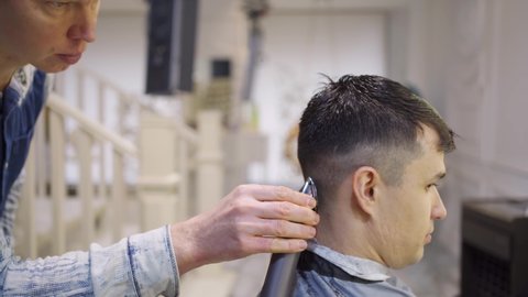 the hairdresser makes a haircut of nape for a brunette man with a hair clipper in a barbershop. professional services. beauty salon for men. cosmetics and products for scalp and hair care.