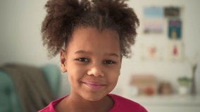 Portrait of little girl talking and having fun while learning online in apartment room spbd. Closeup view of American African child looks forward and speaks with smile, studies remotely and sits at