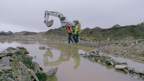 Two Professional Surveyors Panning Precious Metal At Gold Extraction Site. Surveyors With Panning Equipment Extracting Gold Dust. Gold Extraction Surveyors In Protective Gear Washing Mineral Rocks
