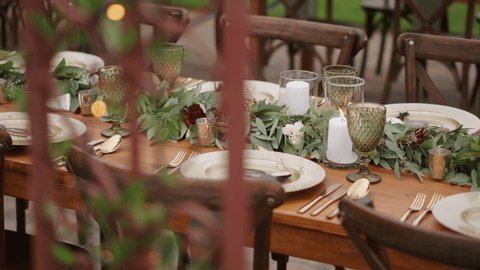 Elegant festive outdoor garden wedding decor with vintage wood chairs and table, golden cutlery decorated with fresh eucalyptus leaves.