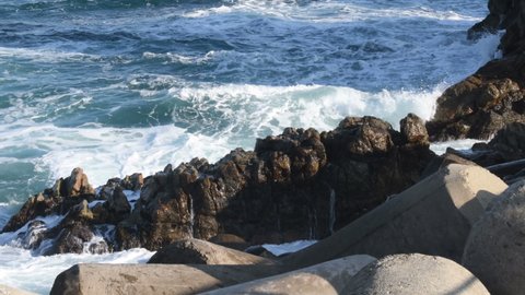 Ocean waves crashing into rocky shore on sunny day.