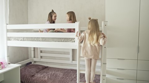 Group of children laughing and playing together on second floor of bunk bed, three girls having fun in bright scandinavian playroom. Family love bonding together concept.