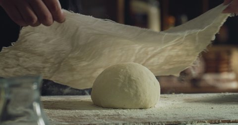 Cinematic close up of professional artisan baker chef covering with rag just prepared loaf of dough for better levitation for preparation of pasta, pizza and other pastries in rustic bakery kitchen.