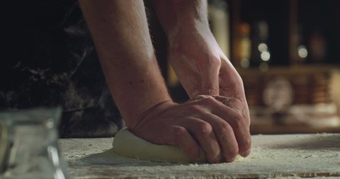 Cinematic close up shot of professional artisan baker chef kneading just prepared loaf of dough for better levitation for preparation of pasta, pizza and other pastries in rustic bakery kitchen.