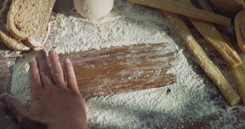 Cinematic close up shot of professional artisan baker chef is making copy space for text with flour on wooden board with bread, loaf and breadsticks on background in rustic bakery kitchen.