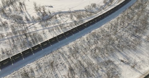 Freight train with empty carriages winding two-sided in wild mountains landscape through a difficult part of Trans Siberian railways - Aerial drone view at winter sunny frozen day