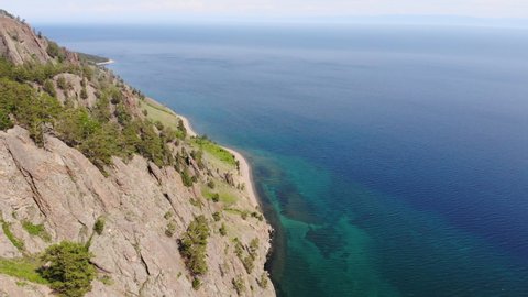 Flying over the rocks and the shore of Lake Baikal from the Skriper cliff in summer.