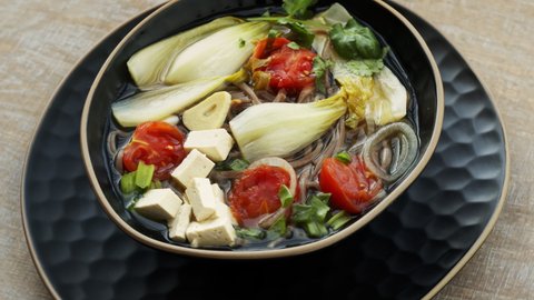 Tom Yum soup with tofu, soba noodles, pak choi cabbage, cherry tomatoes, spring onion and fresh coriander. Thai cuisine.