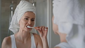Caucasian woman with towel on hair brushing teeth in the bathroom. Shot with RED helium camera in 8K. 