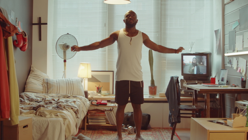 Young African American man stretching shoulders and doing pushups in bedroom at home