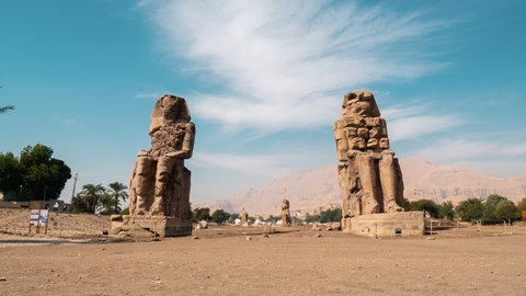 Colossi of Memnon on blue sky. Timelapse. Massive stone statues of Pharaoh Amenhotep III near Mortuary Temple. View from bottom between ancient monuments. Egyptian cultural heritage