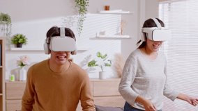 Asian couple playing and enjoying video games with VR head sets at home. Happy couple having fun with virtual reality glasses in living room. Hands moving while playing and greetings at the end. - Powered by Shutterstock - Get 15% off with code: PIKWIZARD15