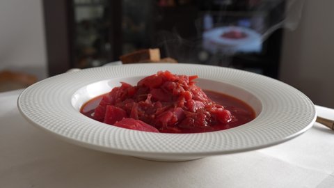 Traditional Ukrainian red soup or borscht  with red beetroot, potato, carrot, cabbage, beans on the white bowl, close up. Plate of red beetroot soup borsch rotates on table. Traditional Ukraine food