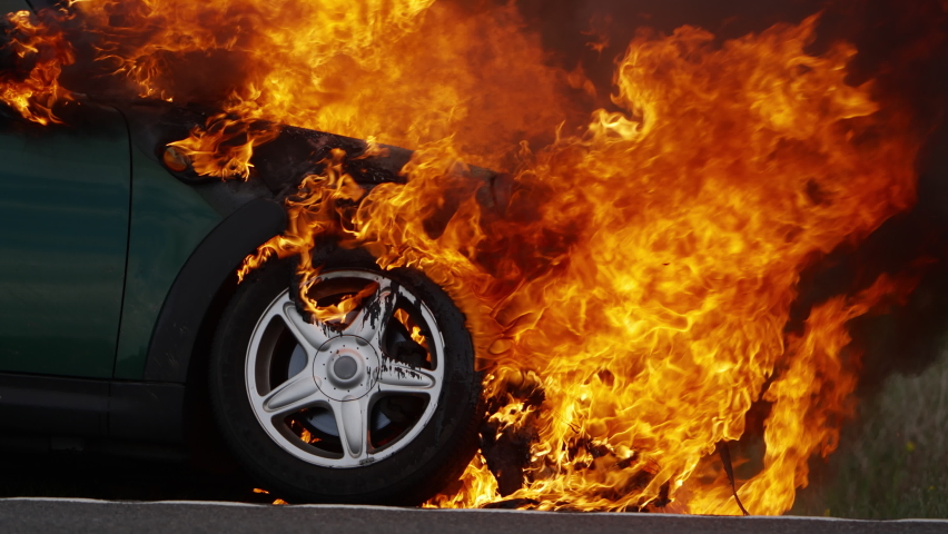 Fire burning a small electric car on the side of the highway after batteries exploded. Fully engulfed in flames and burning out of control. 4K slow motion at 120 fps. Royalty-Free Stock Footage #1088678523