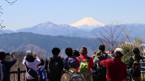 Tourists standing on a viewing platform at the top of Mt Takao taking photos of Mount Fuji in the distance. Japan - 13th April 2019