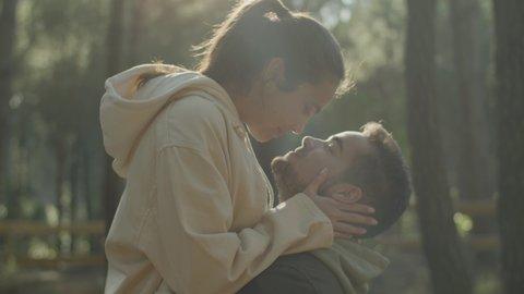 Lovely young couple kissing outdoors while spending time outdoors in nature. Guy holding girlfriend in his arms while girl kissing him gently on the lips. Love, romance, passion concept